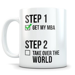 May include: White ceramic mug with black text that reads "STEP 1 GET MY MBA" with a checkmark in a box next to the text. Below the text is "STEP 2 TAKE OVER THE WORLD" with an empty box next to the text.