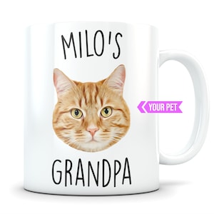 Peut inclure: Mug en céramique blanche avec une image de dessin animé d'un chat roux avec le texte "MILO'S GRANDPA" et un ruban rose avec le texte "YOUR PET" sur le côté.