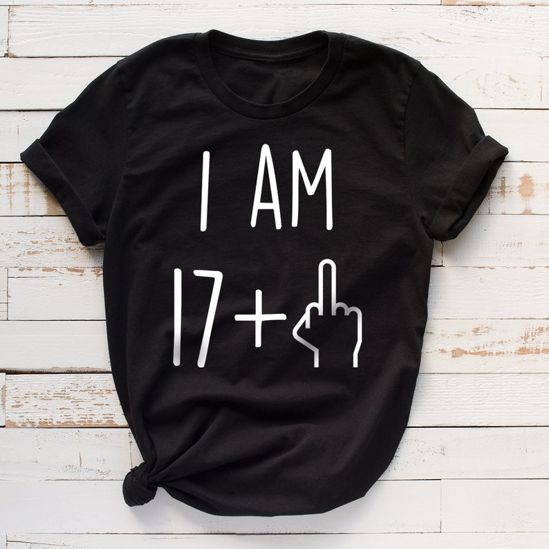 May include: Black t-shirt with white text that reads "I AM 17+" with a middle finger emoji.