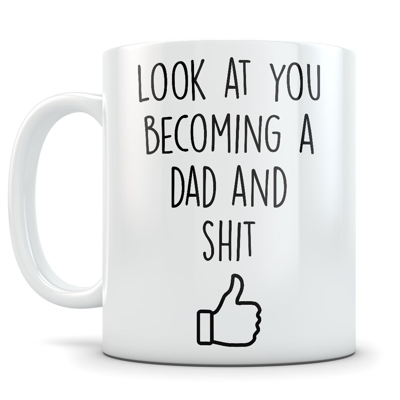 May include: White ceramic coffee mug with black text that reads "Look at you becoming a dad and shit" with a thumbs up emoji.