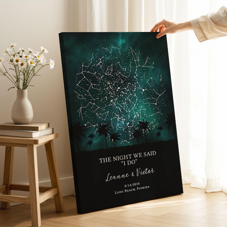 A person is holding up a canvas print of a starry night sky with palm trees in the background.