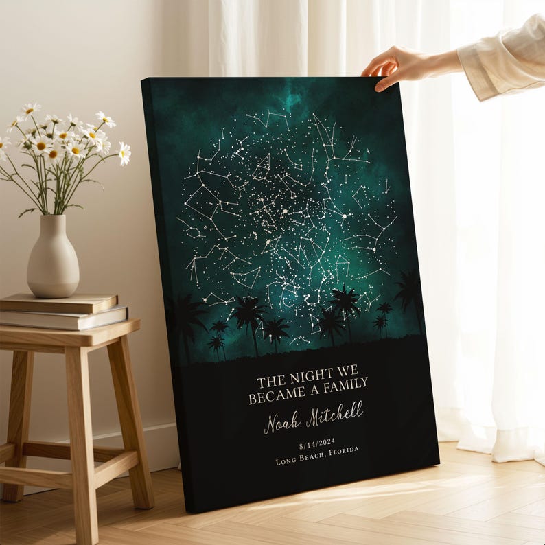 A person's hand is holding a canvas print of a starry night sky with palm trees in the background.