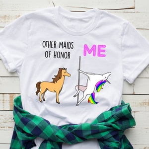 May include: White t-shirt with a graphic of a unicorn and a horse. The text "Other maids of honour" and "ME" is printed on the shirt.