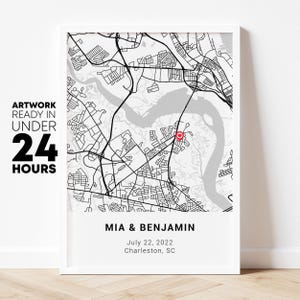 May include: Framed black and white map print featuring a detailed street layout with a red heart-shaped marker. The print includes the names "MIA & BENJAMIN", the date "July 22, 2022", and the location "Charleston, SC". Text on the left says "ARTWORK READY IN UNDER 24 HOURS".