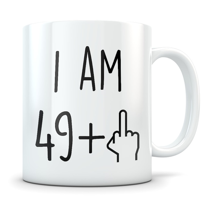 May include: White ceramic coffee mug with black text that reads "I AM 49 +" followed by a black and white illustration of a middle finger.