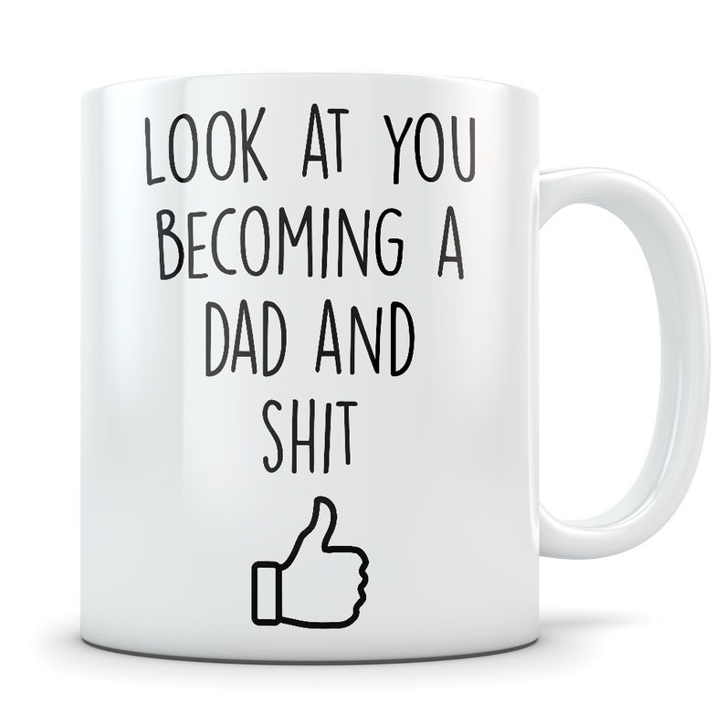 May include: White ceramic coffee mug with black text that reads "Look at you becoming a dad and shit" with a thumbs up emoji.