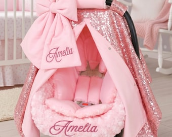 Könnte beinhalten: Rosa Baby-Autositzbezug mit großer Schleife, Pailletten-Baldachin und dem Namen "Amelia" auf der Vorderseite gestickt. Der Sitz hat ein weiches, plüschiges Innenfutter für Komfort und Sicherheit von Säuglingen.