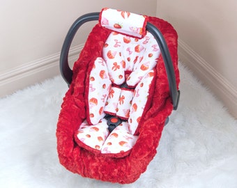 May include: Red plush car seat cover with a white and pink patterned insert featuring strawberries and cupcakes.
