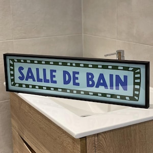 Könnte beinhalten: Ein schwarzes Schild mit einem blauen und weißen Hintergrund und grünem Rand. Das Schild zeigt "Salle de Bain" in blauen Buchstaben.