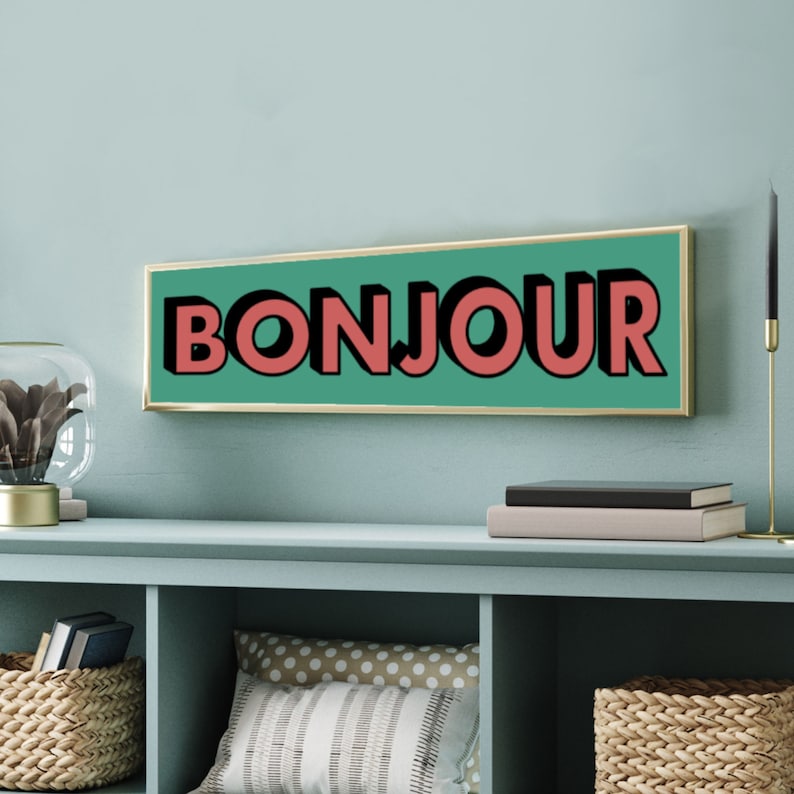 Puede incluir: Un letrero rectangular verde azulado con marco dorado. El letrero dice "BONJOUR" en letras rojas grandes y en negrita.