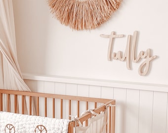 May include: A white canopy crib with a white and brown peace sign patterned quilt. The crib is decorated with a beige and brown lion head wall hanging and a wooden sign that says "Tully".