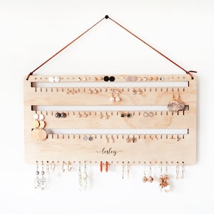 May include: Wooden earring holder with three rows of hooks for studs and a bottom row of hooks for dangling earrings. The holder is personalised with the name "Lesley".