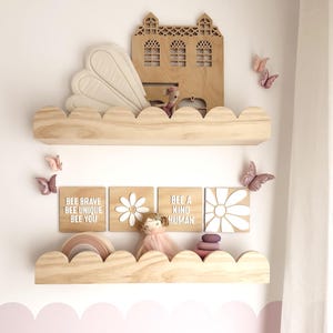 May include: Wooden cloud-shaped shelves with decorative items. Includes a wooden house, butterflies, and square plaques with text: "BEE BRAVE BEE UNIQUE BEE YOU" and "BEE A KIND HUMAN". A doll and rainbow decor are also present.