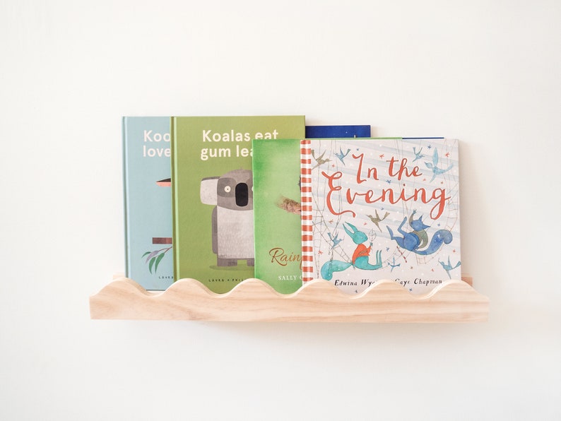 Peut inclure: Une &eacute;tag&egrave;re en bois avec un bord festonn&eacute; pr&eacute;sente une collection de livres pour enfants. Les livres ont des couvertures color&eacute;es avec des illustrations d'animaux et de sc&egrave;nes de nature. Les titres des livres sont "Koo love", "Koalas eat gum lea", "Rain", "In the Evening", et "Edwina Wy Caye Chapman".