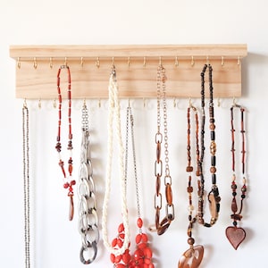 May include: A wooden jewelry organizer with gold hooks, holding a variety of necklaces. The necklaces are made of different materials, including beads, metal, and plastic. The organizer is a great way to keep jewelry organized and tangle-free.
