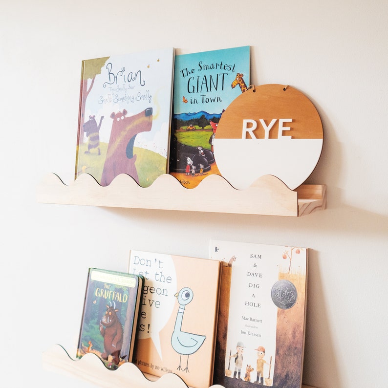 Peut inclure: Deux &eacute;tag&egrave;res en bois aux bords festonn&eacute;s, contenant une vari&eacute;t&eacute; de livres pour enfants. L'&eacute;tag&egrave;re du haut a une pancarte ronde en bois avec le nom "RYE" en lettres blanches. Les livres sur l'&eacute;tag&egrave;re du haut comprennent "Brian", "The Smartest Giant in Town", et "The Gruffalo". Les livres sur l'&eacute;tag&egrave;re du bas comprennent "Don't Let the Pigeon Drive the Bus", "Sam & Dave Dig a Hole", et "The Gruffalo".