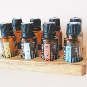 May include: A wooden essential oil rack with eight amber glass bottles. The bottles are labeled with the brand "dōTERRA" and the names "Lemon", "Purify", "On Guard", and "Peppermint". Each bottle contains 15 ml of essential oil.