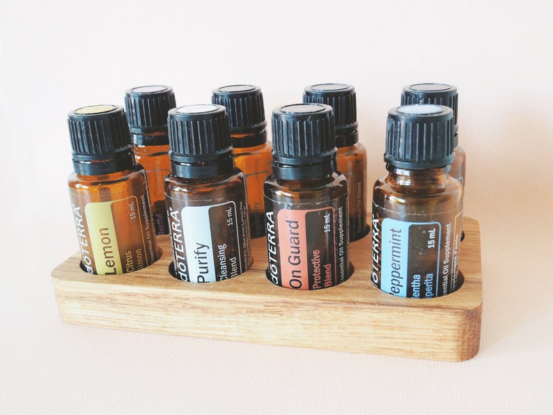 May include: A wooden essential oil rack with eight amber glass bottles. The bottles are labeled with the brand "dōTERRA" and the names "Lemon", "Purify", "On Guard", and "Peppermint". Each bottle contains 15 ml of essential oil.