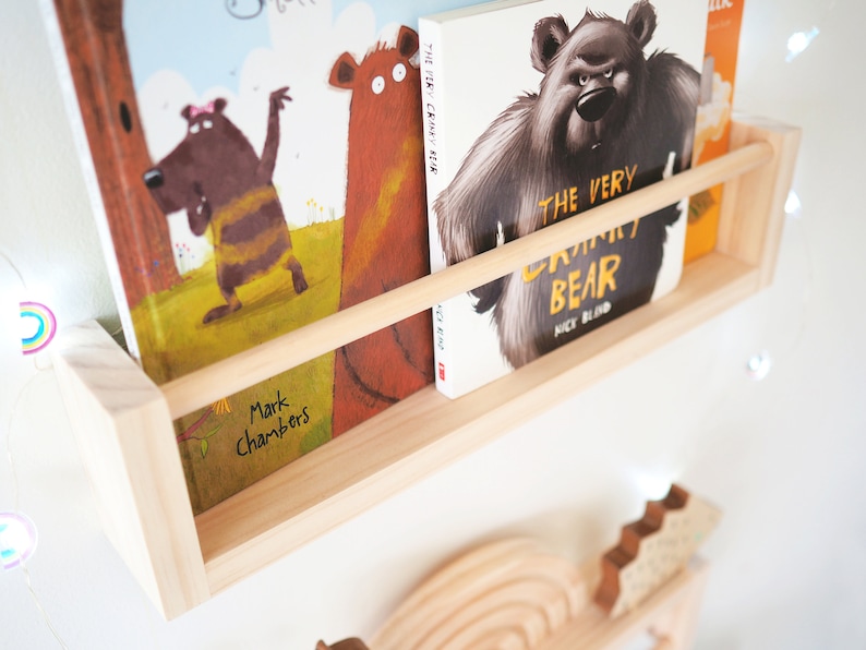 May include: A wooden shelf with two children's books. The book on the left is titled "The Cranky Bear" by Mark Chambers. The book on the right is titled "The Very Cranky Bear" by Nick Bland.