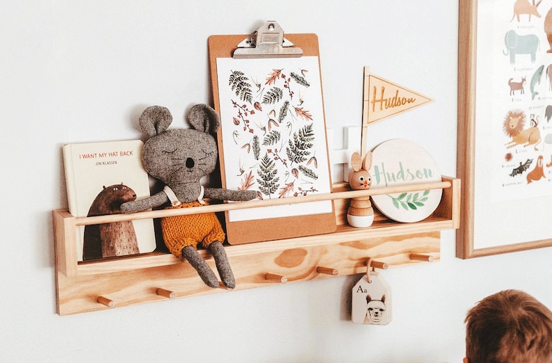 May include: A wooden shelf with a gray stuffed mouse, a book titled "I Want My Hat Back", a clipboard with a botanical print, a wooden bunny toy, a round wooden sign with the name "Hudson" and a wooden tag with the letter "A" and an alpaca illustration.