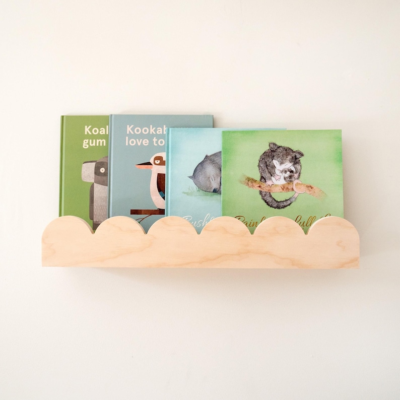 May include: A wooden cloud-shaped shelf holds four children's books with animal illustrations. The books have green, blue, and light green covers. The shelf is made of light-colored wood and is mounted on a white wall.