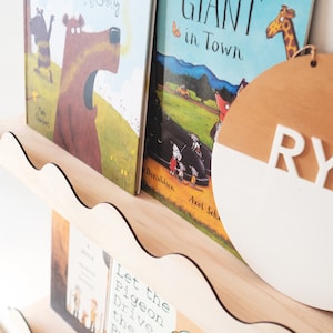 Peut inclure: Une &eacute;tag&egrave;re en bois avec un bord festonn&eacute; pr&eacute;sente une collection de livres pour enfants. Les livres sont intitul&eacute;s "A Hole is to Dig", "Let the Pigeon Drive the Bus", "Giant in Town" et "A Bear Called Paddington". Un panneau rond en bois avec les lettres "RY" peintes en blanc est sur l'&eacute;tag&egrave;re.