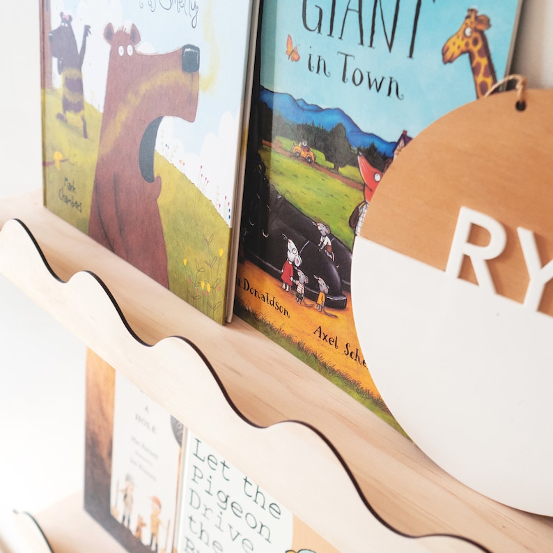 Peut inclure: Une &eacute;tag&egrave;re en bois avec un bord festonn&eacute; pr&eacute;sente une collection de livres pour enfants. Les livres sont intitul&eacute;s "A Hole is to Dig", "Let the Pigeon Drive the Bus", "Giant in Town" et "A Bear Called Paddington". Un panneau rond en bois avec les lettres "RY" peintes en blanc est sur l'&eacute;tag&egrave;re.