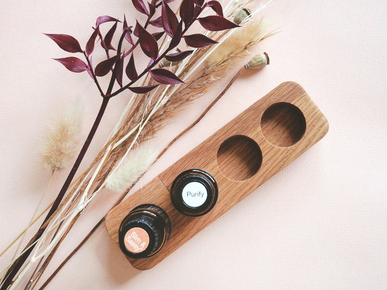 May include: Wooden essential oil holder with two slots. The holder is made of light brown wood and has two round slots for essential oil bottles. The bottles are labeled "Slim & Sassy" and "Purify".