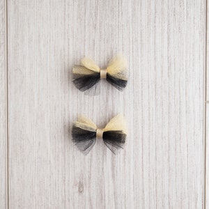 May include: Two black and gold tulle bows with a gold center. The bows are on a light wood background.