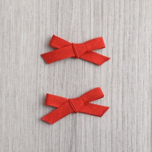 May include: Two red fabric bows on a woodgrain background.
