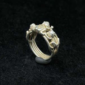 Puede incluir: Un anillo de plata con un diseño de tres figuras entrelazadas. El anillo está hecho de múltiples bandas que están conectadas entre sí.