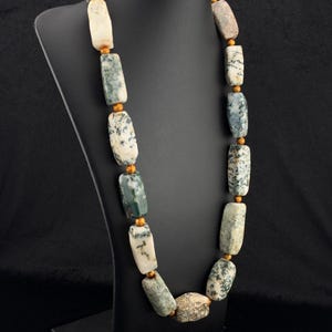 May include: A necklace featuring rectangular, polished stone beads with white, gray, and dark green moss-like inclusions. The stones are separated by small, round, textured gold-colored metal spacer beads, creating a repeating pattern along the strand.