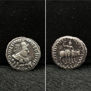 May include: Two silver coins. One coin features a bust of a man with a crown and beard, surrounded by text. The other coin depicts a figure riding an animal, also with surrounding text. Both coins have a worn, antique appearance.