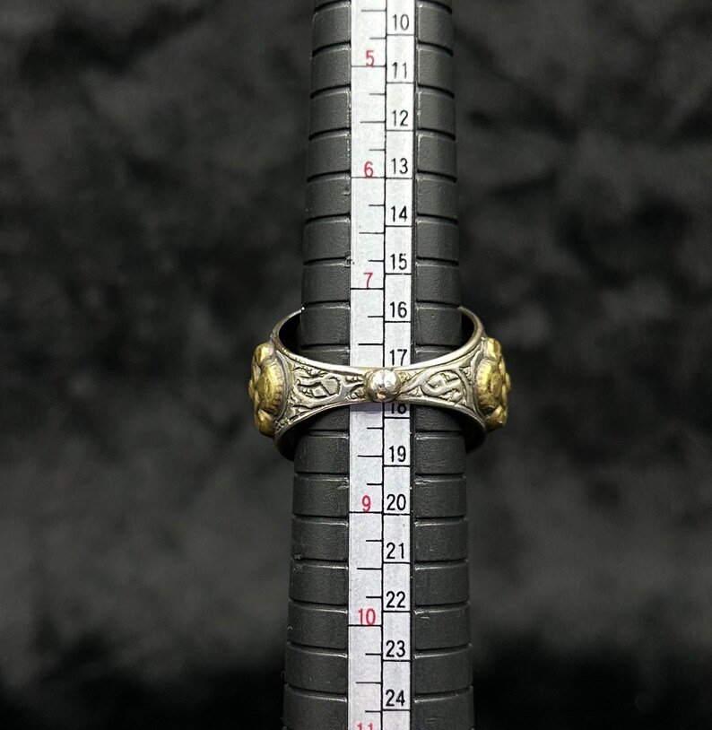 May include: A silver and gold ring with intricate designs and a small pearl accent. The ring is measured against a ruler, showing a size of 18.