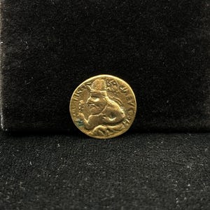 May include: A gold coin with a profile of a person wearing a helmet. The coin has text around the edge.
