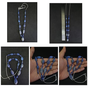 Pode incluir: Um colar de contas de lapis-lazúli azul e branco com um pingente. O colar é feito de contas ovais com linhas brancas que as atravessam. O pingente é uma conta oval maior com linhas brancas que a atravessam.