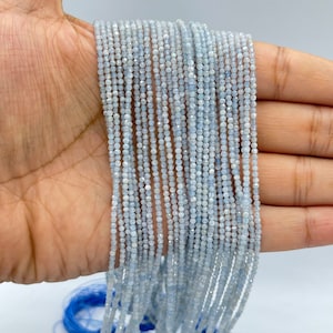 Puede incluir: Una hebra de cuentas de piedras preciosas de color azul claro. Las cuentas son pequeñas y redondas, y están enhebradas en un alambre fino. Las cuentas están dispuestas en línea recta, y todas son del mismo tamaño y forma.