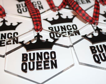 May include: Clear acrylic hexagon-shaped ornaments with the words "Bunco Queen" in bold black letters, topped with a black crown. Each ornament is strung with a red and black plaid ribbon, perfect for gifting or decorating.