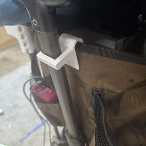 May include: A white plastic stroller accessory, designed to clip onto the stroller frame. The accessory is attached to a brown fabric stroller bag with black mesh pockets. The stroller frame is black.