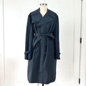May include: A black double-breasted trench coat with a belted waist and notched lapels. The coat features a classic design with button closures and long sleeves. The coat is displayed on a mannequin.