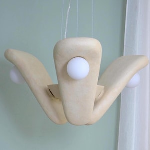 May include: A contemporary, cream-coloured chandelier with an unusual, organic design. The fixture has three curved, petal-like arms, each holding a spherical, white light. The light hangs from thin wires, creating a floating effect.
