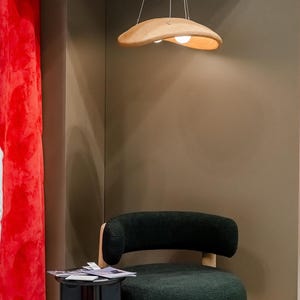 May include: A black armchair with a wooden base and a light wood, double-bulb pendant light hanging above it.