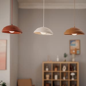 Pode incluir: Tr&ecirc;s lumin&aacute;rias pendentes com abajures texturizados em forma de tigela nas cores vermelho, branco sujo e castanho claro. Cada lumin&aacute;ria pende de um fio fino e apresenta uma fonte de luz central. As lumin&aacute;rias est&atilde;o suspensas em uma sala com uma paleta de cores neutras.