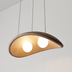 May include: A modern pendant light fixture with a brown, curved, ceramic shade and two white globe light bulbs.