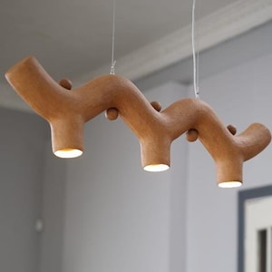 May include: A brown, wavy, ceramic pendant light fixture with three bulbs. The light fixture is hanging from the ceiling in a room with a wooden dresser and a chair.
