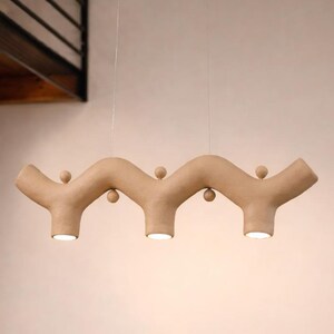May include: A beige, wavy, horizontal pendant light fixture suspended by thin wires. The fixture features three downward-facing circular light sources and small spherical decorative accents positioned along the top and bottom curves of the structure.