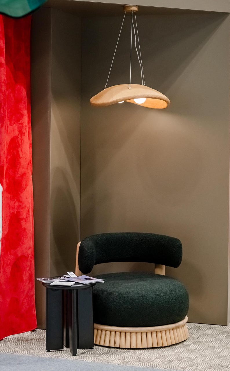 May include: A black armchair with a wooden base and a light wood, double-bulb pendant light hanging above it.