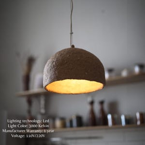 May include: A pendant light fixture with a brown, dome-shaped shade. The interior of the shade glows with a warm, yellow light. The fixture hangs from a thin cord. The text on the image says: Lighting technology: Led, Light Color: 3000 Kelvin, Manufacturer Warranty: 1 year, Voltage: 110V/220V.