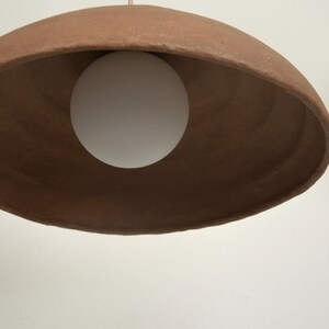 May include: A terracotta-colored pendant light with a white globe light bulb hanging from a thin wire.
