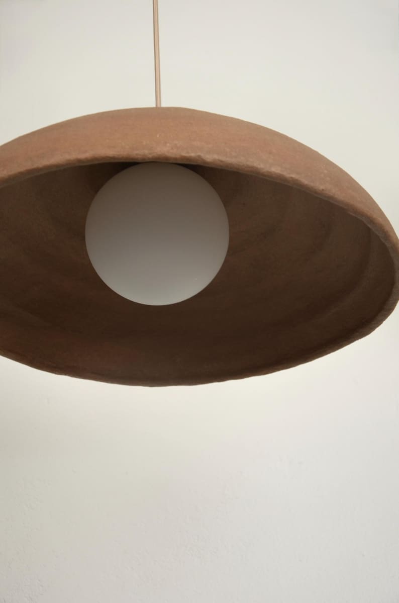 May include: A terracotta-colored pendant light with a white globe light bulb hanging from a thin wire.